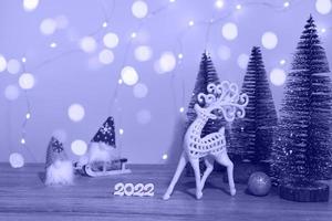 Christmas and New Year's decor. Christmas deer, numbers 2022, gnome on a sled and Christmas trees on a wooden background with Christmas lights. Christmas card photo