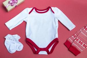 Christmas white baby bodysuit mockup on a colored background close up with red New Year's pants Mockup of clothes for newborns. With copy space photo