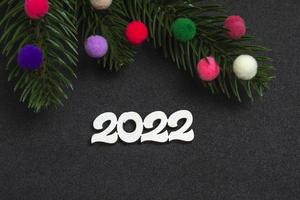 Christmas card. Flatley branches of a Christmas tree colorful fur toys with the numbers 2022 on a black background. photo