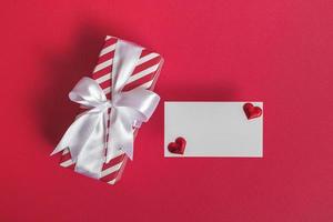 Gift box with blank card and hearts on a red background. Valentine's day concept. photo