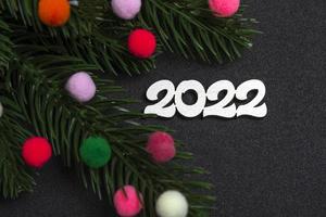 tarjeta de Navidad. flatley ramas de un árbol de navidad juguetes de pieles de colores y el número 2022 sobre un fondo negro. foto