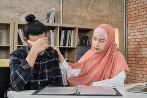 A young female startup work partner who is an Islamic person encourages and comforts a male colleague from being sad and stressed in the small workplace, e-commerce business office. photo
