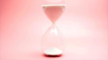 Close up, The hourglass and white sand are in a glass jar. The sand is all flowing down, time is running out. On the pink background. video