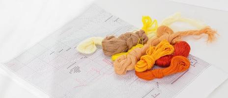 color threads for embroidery and printed scheme on a white table. hobby and leisure for relaxation and mind balance. banner size. set of multicolored floss photo