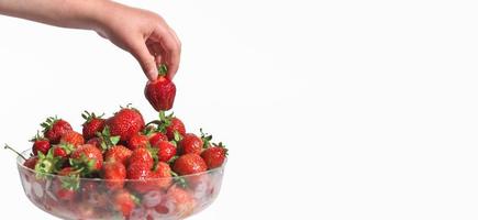 kids hand taking a strawberry on a white background. copy space. vitamins and antioxidants. bowl full of fresh garden strawberries