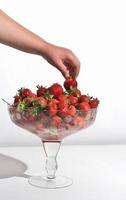 kids hand taking a strawberry on a white background. copy space. vitamins and antioxidants. bowl full of fresh garden strawberries, vertical size