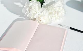 open blank diary or notebook on a table with white peonies. mockup for inscription. good morning concept photo