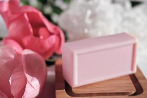 barra rosa de jabón de tocador con flores en la jabonera de madera. producto de belleza perfumado con fragancia de peonía. cuidado de la belleza y concepto de spa. foto