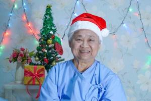Paciente asiático mayor o mayor de la mujer de la señora mayor con el sombrero del ayudante de santa claus en la fiesta navideña del festival de la celebración de la Navidad y del año nuevo en el hospital. foto