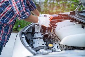 Asian auto mechanic check for repair under the hood of broken down car on the side of the road. photo