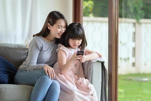 Madre asiática y su hija disfrutan de usar Internet a través de teléfonos inteligentes en casa