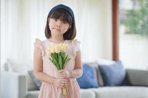 Retrato de flor asiática de holdign de niña linda con feliz sonrisa encantadora en la sala de estar en casa.