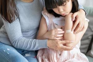 Madre asiática poniendo corte vendaje adhesivo de yeso a su hija en casa foto