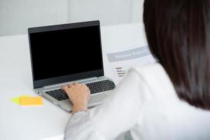 Vista posterior de la mujer de negocios que usa la computadora portátil con pantalla en negro en la oficina. Diseño fotográfico con espacio de copia para maquetas de concepto de negocio