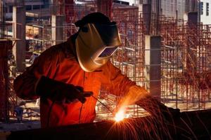 Industrial worker welding steel structure for infrastructure building project with construction site in background. photo