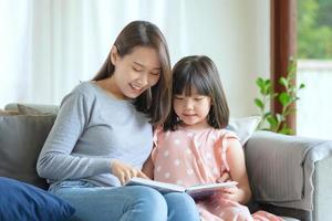 Feliz madre asiática enseñando a su linda hija a estudiar en la sala de estar en casa foto