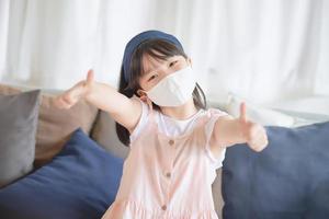 linda niña asiática con mascarilla higiénica para prevenir el coronavirus o el brote de covid-19 mantener el distanciamiento social y quedarse en casa. foto