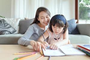 Madre asiática enseñando a su linda hija a estudiar en la sala de estar en casa foto