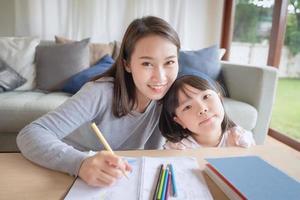 Feliz madre asiática enseñando a su linda hija a estudiar preescolar en la sala de estar en casa