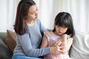 Madre asiática poniendo corte vendaje adhesivo de yeso a su hija en casa