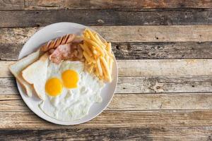 Top view of american breakfast with scrambled eggs,bacon,toast,french fries and sausage on wooden table background. photo