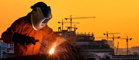 Trabajador industrial soldadura de estructura de acero para proyecto de construcción de infraestructura con sitio de construcción en segundo plano.