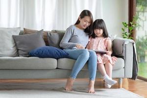 Feliz madre asiática enseñando a su linda hija a estudiar en la sala de estar en casa foto