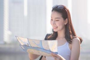 hermosa mujer asiática turista en solitario mirando el mapa en busca de turistas lugares de interés turístico. viajes de vacaciones en verano. foto