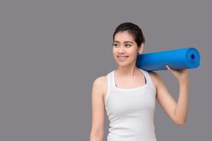 mujer asiática sosteniendo su estera de yoga en el gimnasio de deporte saludable. el yoga y la meditación tienen buenos beneficios para la salud. concepto de fotografía para el deporte de yoga y estilo de vida saludable foto
