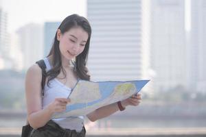 hermosa mujer asiática turista en solitario mirando el mapa en busca de turistas lugares de interés turístico. viajes de vacaciones en verano. foto