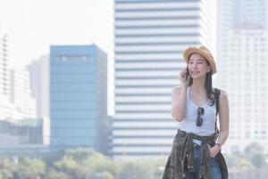 hermosa mujer asiática turista en solitario sonriendo y disfruta tomando a través de teléfono móvil en el centro de la ciudad. viajes de vacaciones en verano. foto