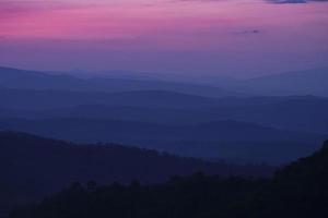 Nature landscape background beautiful view of the morning fog filling the valleys of smooth hills mountain range layer dark blue forest sunrise and sunset in mountains with purple sky dramatic photo