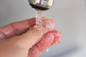 Detalle del concepto de higiene chorro de agua en el baño: lavarse las manos bajo el grifo de agua o el grifo foto