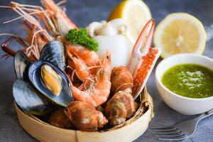 Fresh shrimps prawns squid mussels  spotted babylon shellfish crab and seafood sauce lemon on plate black stone background - Cooked steamer food served seafood buffet concept photo