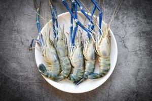 Langostinos camarones frescos para cocinar sobre fondo oscuro en el restaurante de mariscos camarones crudos azul sobre placa blanca. foto