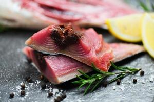 Raw fish seafood on black plate background , Longtail tuna , Eastern little tuna fillet ingredients for cooking food - fresh fish fillet sliced for steak or salad with herbs spices rosemary and lemon
