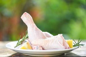 rosemary chicken meat - fresh raw chicken leg on plate and wooden table on nature background photo