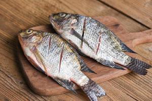 Pescado de tilapia fresca para cocinar alimentos - dos peces de agua dulce de tilapia del Nilo crudos sobre tabla de madera foto