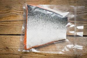 Filete de salmón envasado en plástico envasado al vacío en el embalaje vender en el supermercado - Filete de pescado de salmón crudo fresco sobre fondo de madera foto