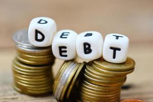 Debt concept with block debt and stacked coins on wooden table background photo