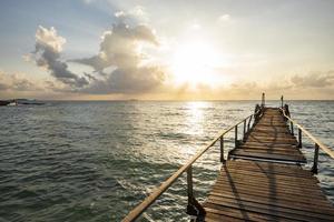 increíble playa tropical de arena con silueta puente de madera fuera de la playa paseo marítimo tropical o pasarela de madera hacia el horizonte en el mar océano paraíso paisaje, amanecer o atardecer mar cielo dramático foto