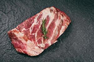 Costillas de cerdo carne cruda sobre fondo de placa negra - costillas de cerdo frescas para cocinar asado o asado, hueso de cerdo con romero foto