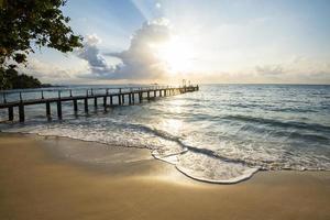 increíble playa tropical de arena con silueta puente de madera fuera de la playa paseo marítimo tropical o pasarela de madera hacia el horizonte en el mar océano paraíso paisaje, amanecer o atardecer mar cielo dramático foto