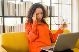 Latin woman working with laptop on sofa with tired feeling photo