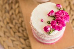 A small cake of white and pink decorated with flowers and berries photo