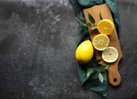 Lemons and green leaves on bright black background. Top view flat lay copy space. Lemon fruit citrus minimal concept vitamin C. photo