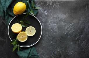 Lemons and green leaves on bright black background. Top view flat lay copy space. Lemon fruit citrus minimal concept vitamin C. photo