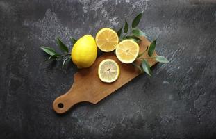Lemons and green leaves on bright black background. Top view flat lay copy space. Lemon fruit citrus minimal concept vitamin C. photo
