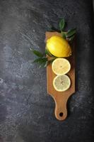 Lemons and green leaves on bright black background. Top view flat lay copy space. Lemon fruit citrus minimal concept vitamin C. photo