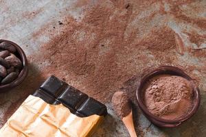 Barra de chocolate oscuro con granos de cacao en polvo esparcidos cuenco como telón de fondo rústico